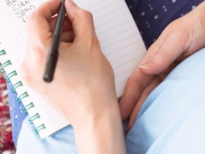 אישה הרהמניחה יד על בטנה וכותבת במחברת בידה השניה