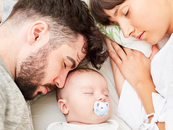 זוג הורים ישנים במיטתם יחד עם תינוקם