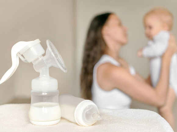 בקבוק חלב אם עם אמא ותינוק ברקע
