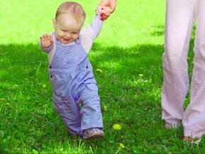 פעוט הולך על הדשא ואוחז בידה של אימו
