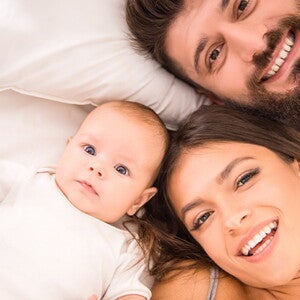 זוג הורים ותינוק מחייכים למצלמה