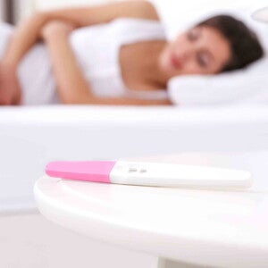 אישה שוכבת על צידה במיטתה כשלפניה מונחת בדיקת הריון ביתית