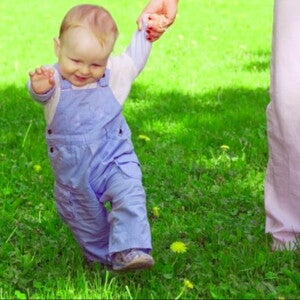 פעוט הולך על הדשא ואוחז בידה של אימו