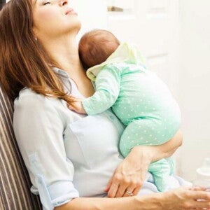 אמא מנמנמת בישיבה בעודה מחזיקה את ביתה