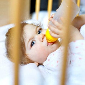 תינוק אוכל מבקבוק מבעד לסורגי מיטת התינוק