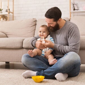 אב ומאכיל את בנו על שטיח בסלון