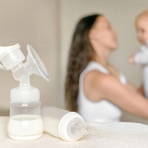 בקבוק חלב אם עם אמא ותינוק ברקע