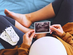 מבט מלמעלה על אישה עם בטן הריונית בעוד היא מסתכלת על תמונת US של העובר שלה