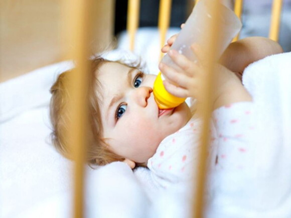 תינוק אוכל מבקבוק מבעד לסורגי מיטת התינוק