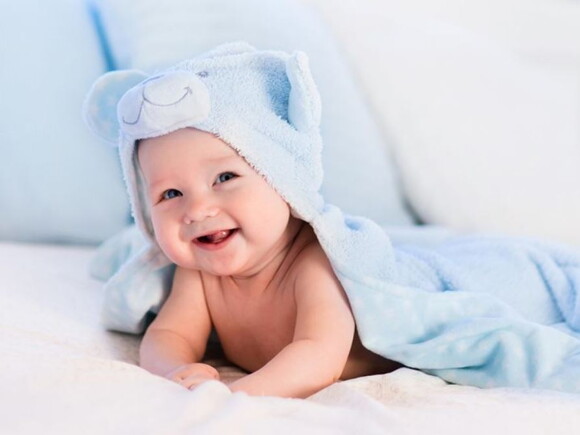 תינוק עטוף מגבת כחולה מחייך ללא שיניים
