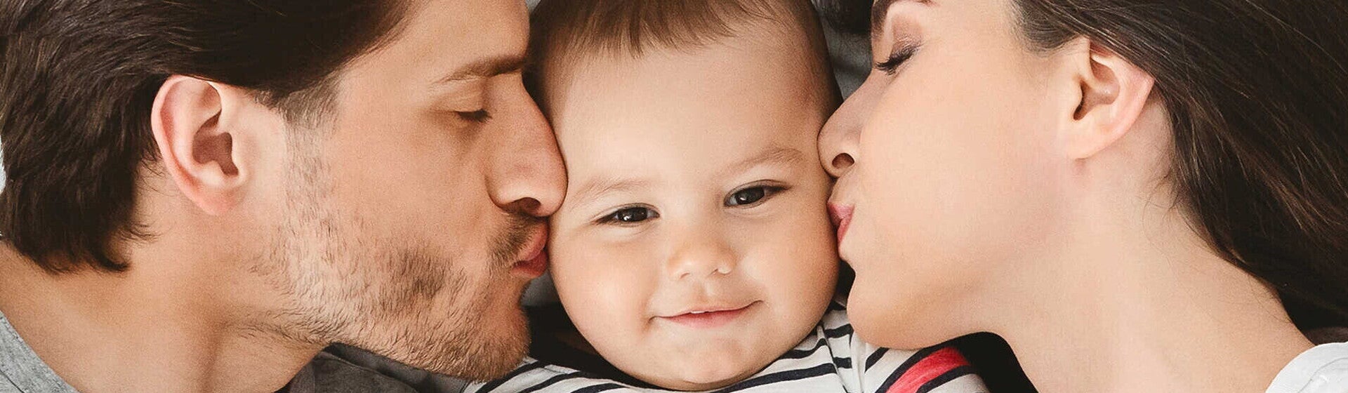 זוג הורים מנשקים עם תינוקם משני צידיו כשהוא שמח במרכז